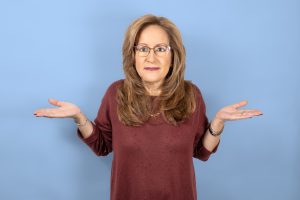 Woman shrugging shoulders with open hands up, blue studio background.