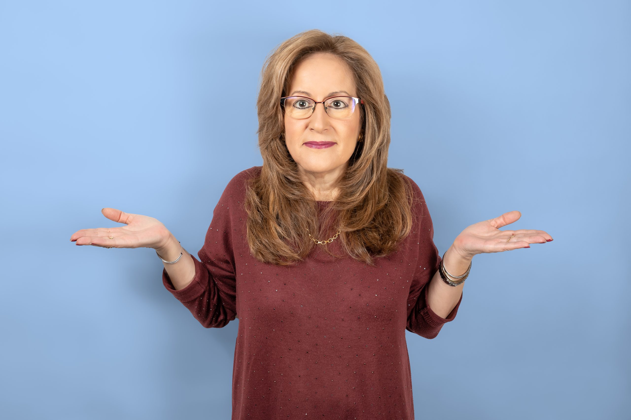 Woman shrugging shoulders with open hands up, blue studio background.